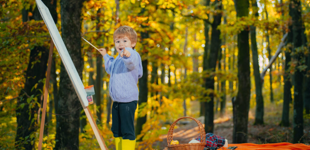 A young boy painting out side in the fall time at a large easel. 