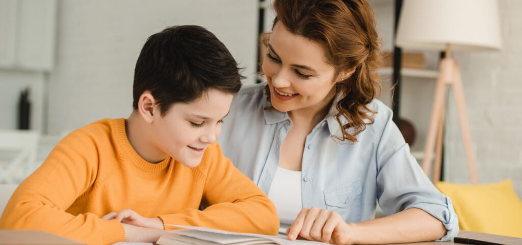 A young boy sitting with his mother reading and discussing a book together. 