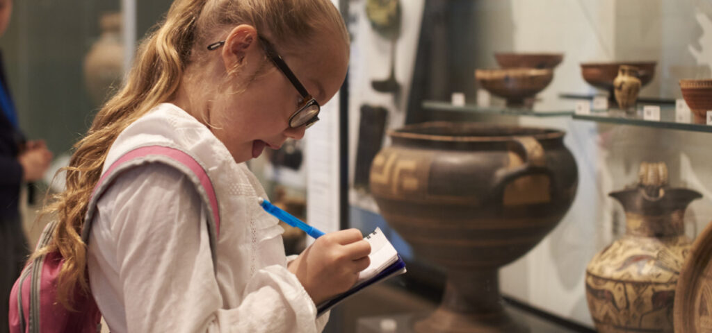 A young girl taking notes at a museum with excitement on her face. 