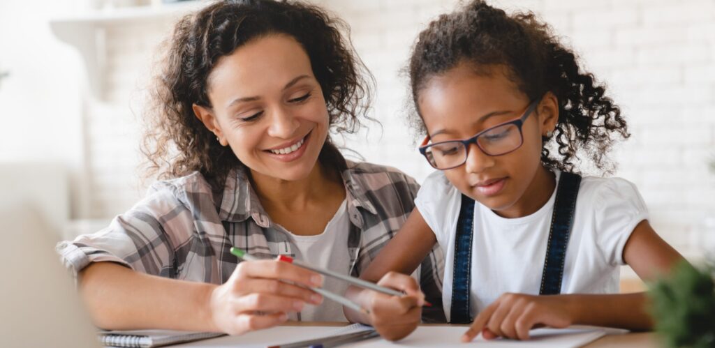 A mom and her daughter writing on a piece of paper at the kitchen table. 