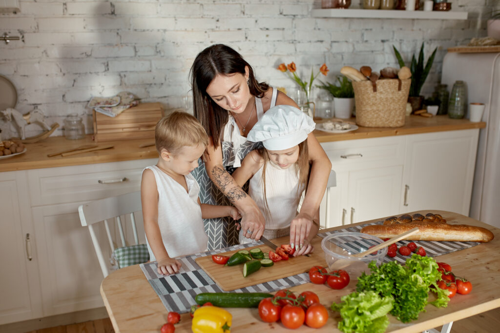 Two children and their mother cutting veggies while preparing a meal. 