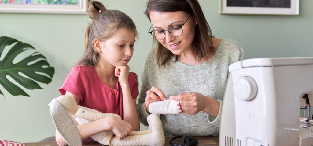 A young girl sewing with her mothers help. 