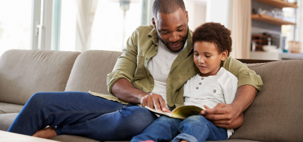 Boy sitting on the couch reading with his father. 