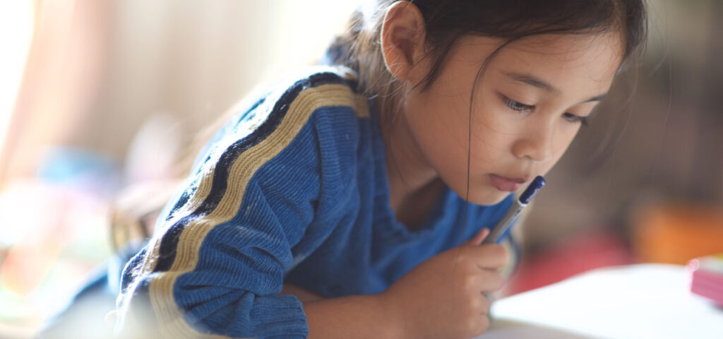 A young girl looking at her notebook with a pen in her hand. 