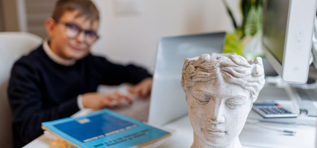 A child at a computer learning about world history in the background of a head sculpture. 