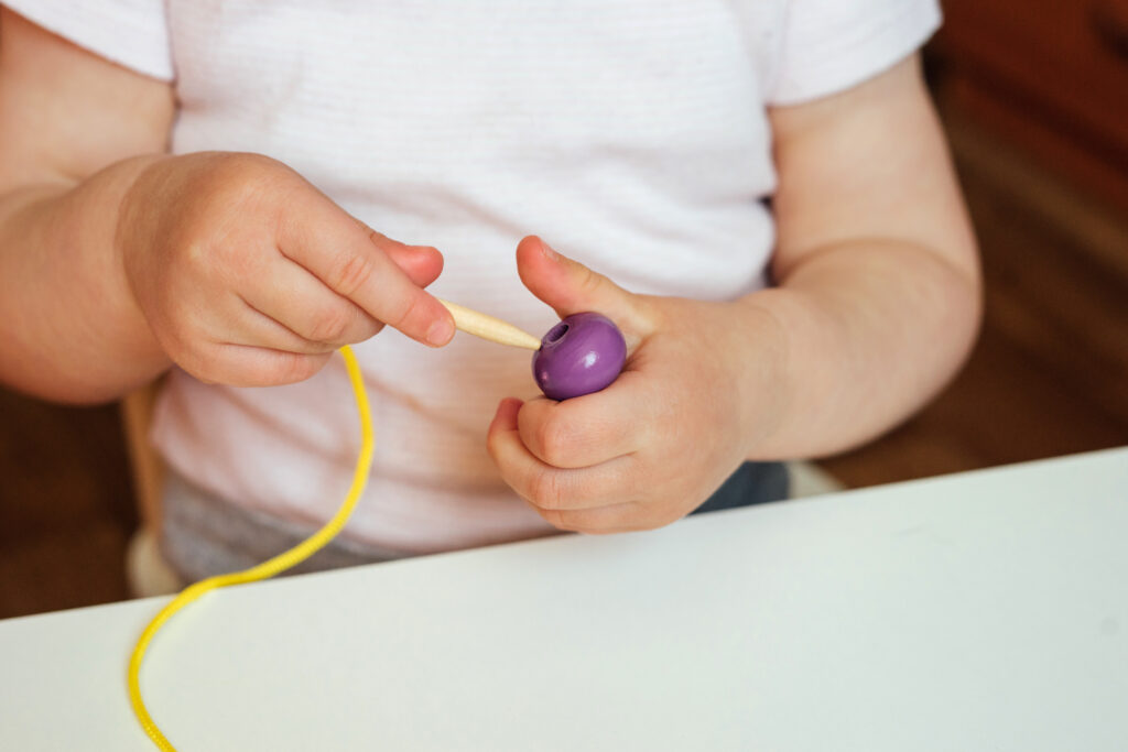 Preschooler trying to fit a string through a bead. 